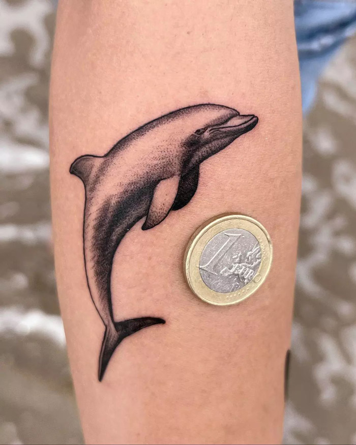 Dolphin tattoo on forearm beside a Euro coin, showcasing animal tattoo ideas for inspiration.