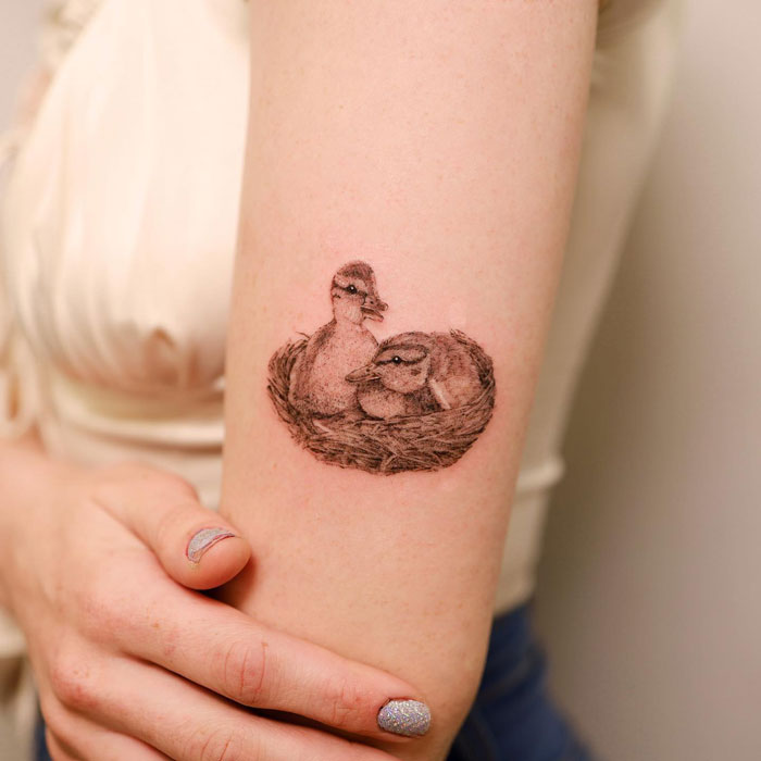 Animal tattoo of two ducklings in a nest on a person's arm.