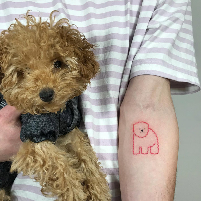 Curly-haired dog held by a person with a matching cute animal tattoo on their arm.
