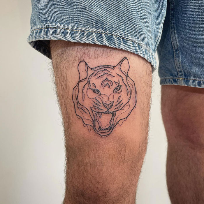 Animal tattoo of a realistic tiger face on a person's thigh, showcasing simplicity.