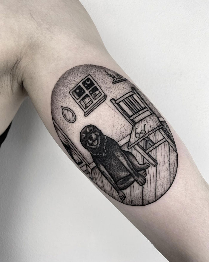 Black and white animal tattoo on arm, featuring a dog sitting in a detailed room setting.
