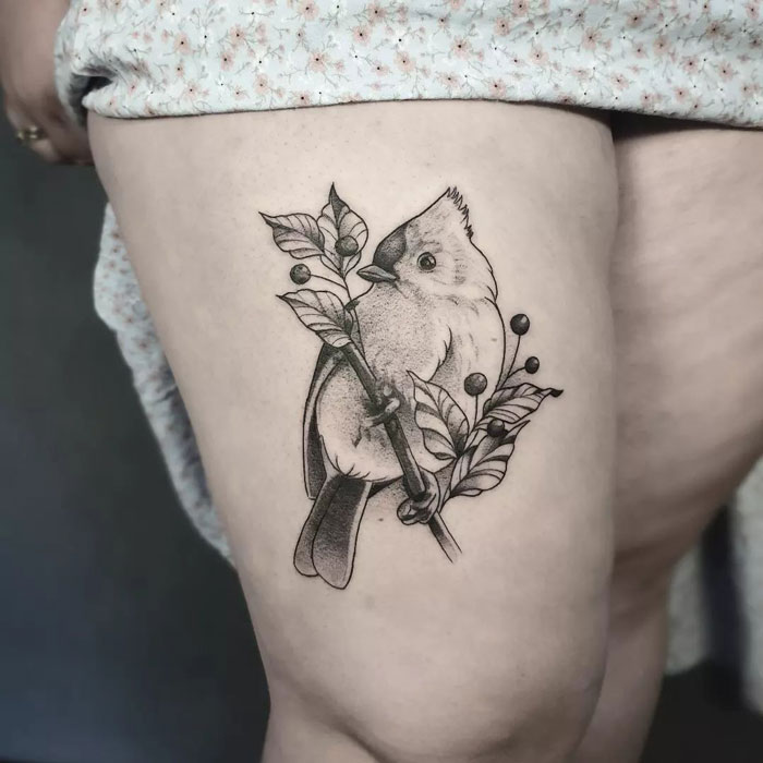 Bird tattoo on thigh with detailed leaves and branches, showcasing animal tattoo artistry.
