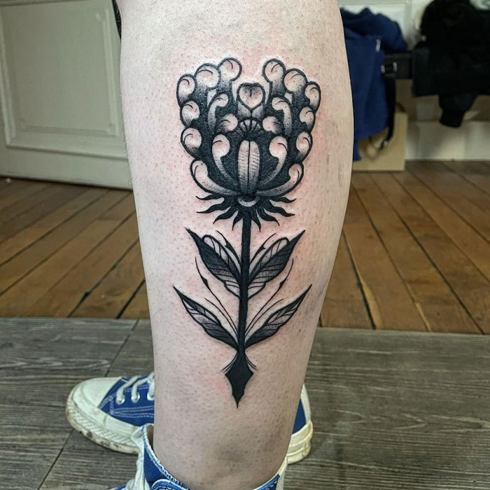 Unique calf tattoo featuring a bold black floral design on a person's leg.
