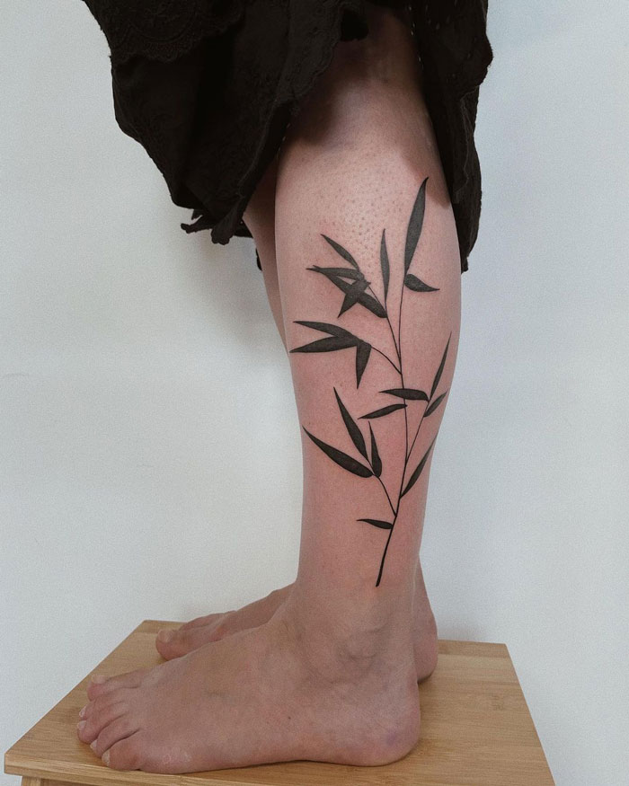 Calf tattoo featuring a black leafy branch design, showcasing a unique and artistic style.
