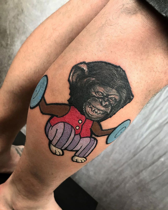 Unique calf tattoo of a cartoon monkey with cymbals, wearing a red vest and striped pants.