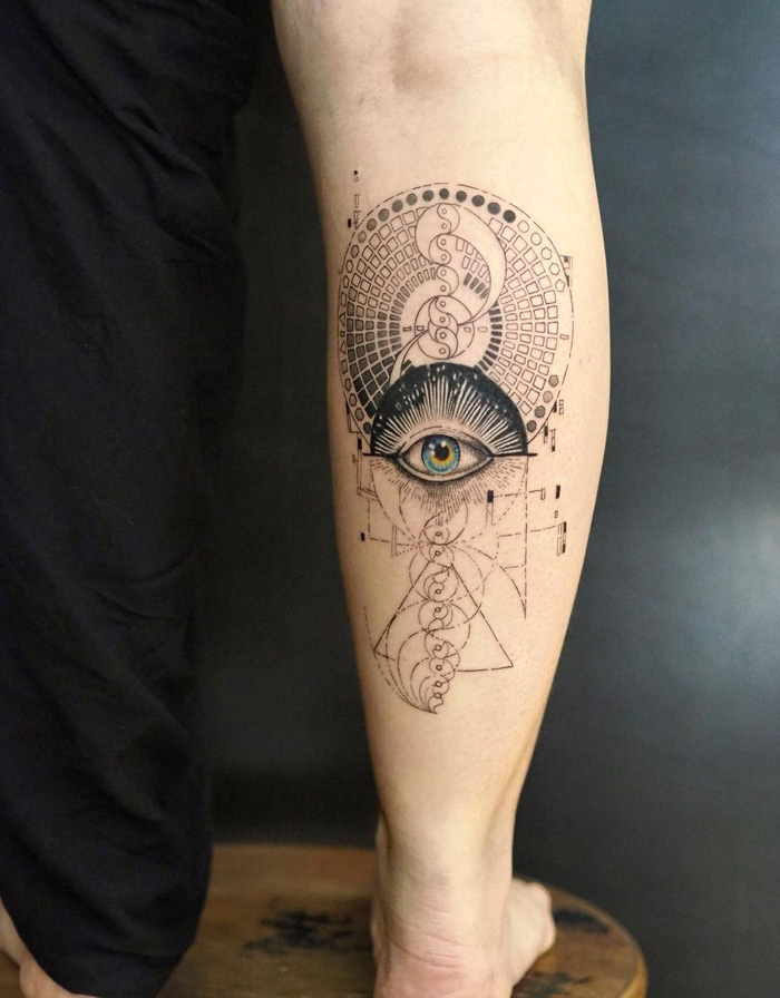 Unique calf tattoo featuring a geometric design with a central eye motif, blending intricate patterns and lines.