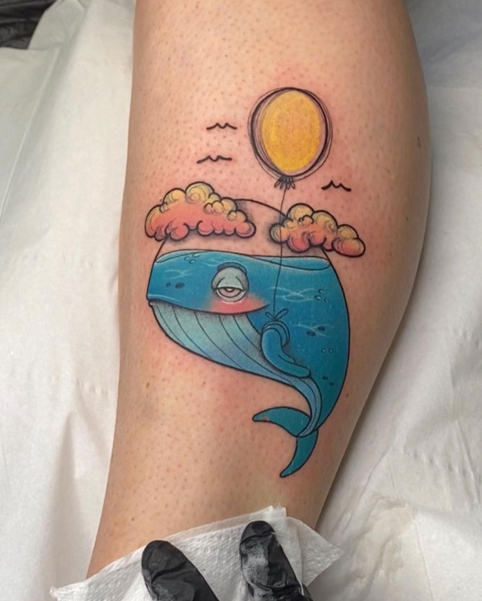 Calf tattoo of a blue whale with clouds and a yellow balloon, showcasing a unique and cool design.