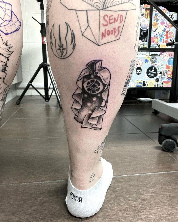 Unique calf tattoo featuring an abstract, cape-wearing figure with geometric elements.