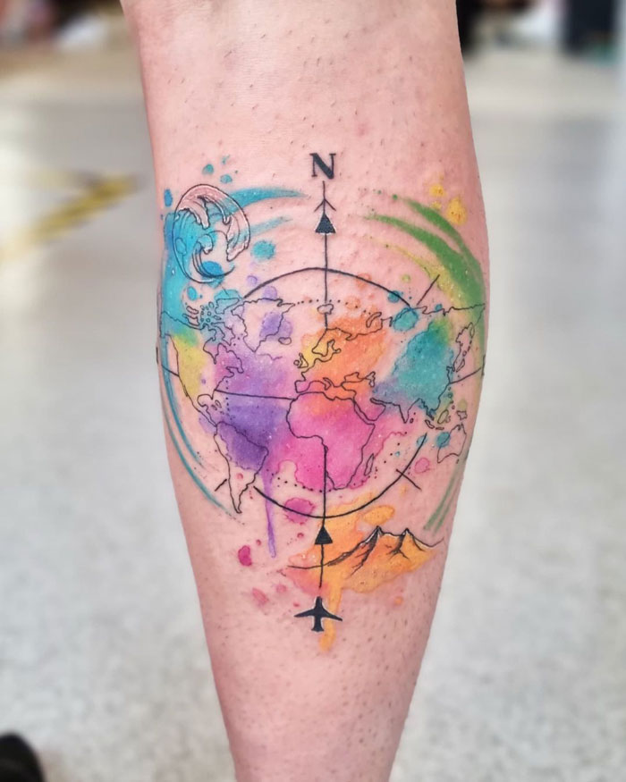 Colorful map-themed calf tattoo with compass and watercolor design, showcasing unique travel inspiration.