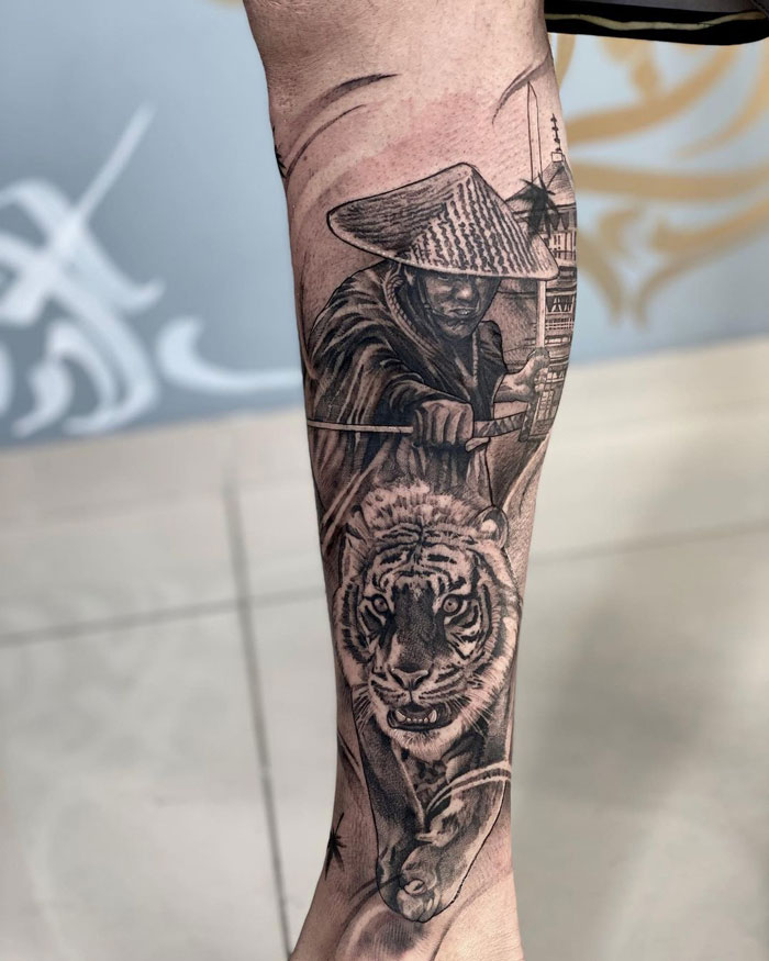 Calf tattoo featuring a warrior with a traditional hat and a fierce tiger, showcasing unique and cool design elements.