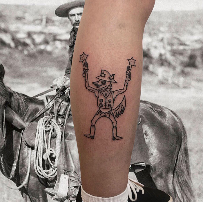 Unique calf tattoo featuring a cowboy-themed cartoon character with pistols, set against a vintage cowboy image.