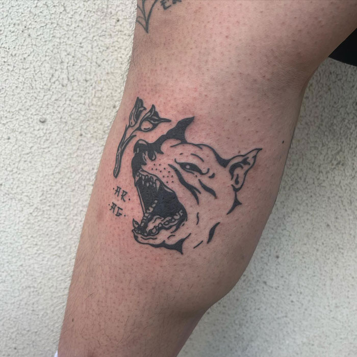 Black ink calf tattoo featuring a snarling dog head and a small flower, showcasing unique tattoo artistry.