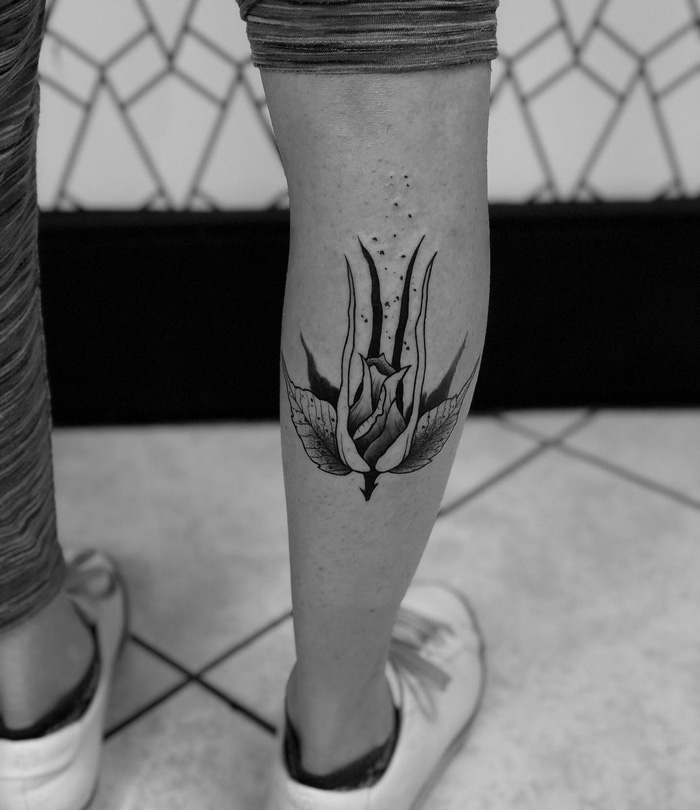 Unique calf tattoo featuring a stylized floral design, showcasing intricate black ink details and artistic flair.