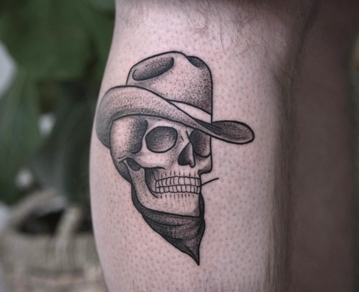 Cowboy skull calf tattoo, featuring a detailed design with a hat and bandana on the leg.