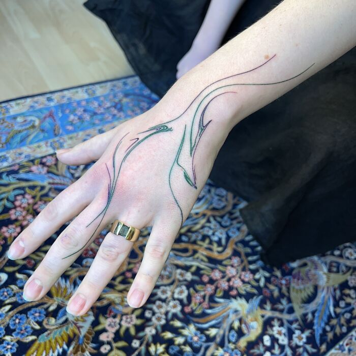 Hand with flowing tattoo design inspired by traditional marbling on a patterned rug.