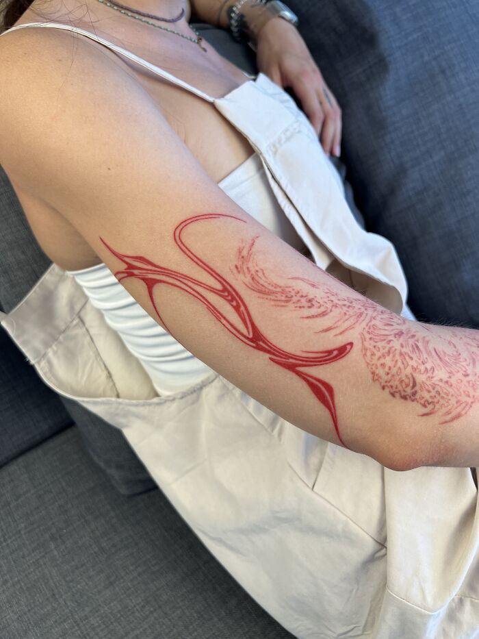 A red flowing tattoo design inspired by traditional marbling on a person's arm, wearing a white top.