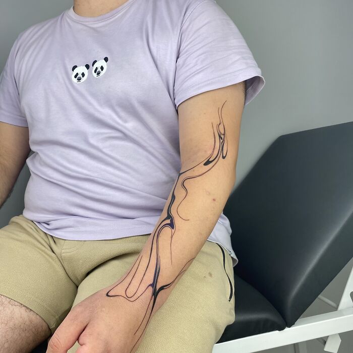 Man with a flowing tattoo design inspired by Sernakkab marbling on his arm, wearing a panda shirt and beige shorts.