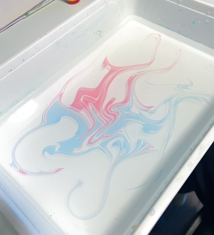 Fluid marbling art with pink and blue swirls in water, reminiscent of sernakkab technique.