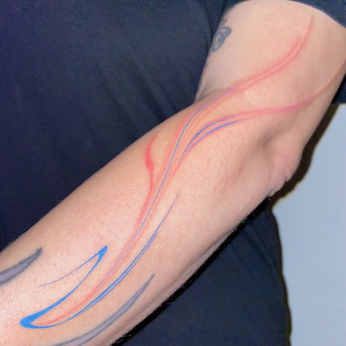 Arm with flowing tattoo design in red and blue, inspired by traditional marbling techniques.