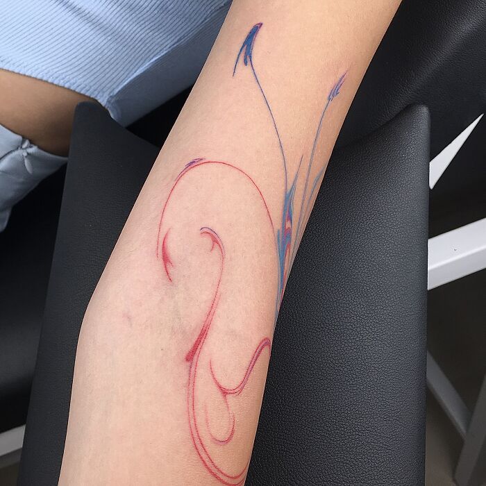 Arm with flowing tattoo design inspired by traditional Sernakkab marbling, featuring red and blue swirls.