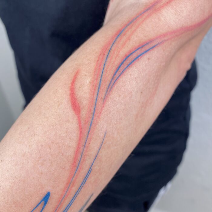 Flowing tattoo designs with red and blue marbling lines on a forearm.