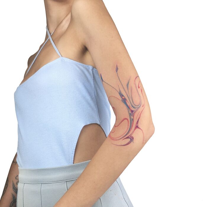 A person showcases a colorful marbling tattoo on their arm, wearing a light blue top with cut-out sides.