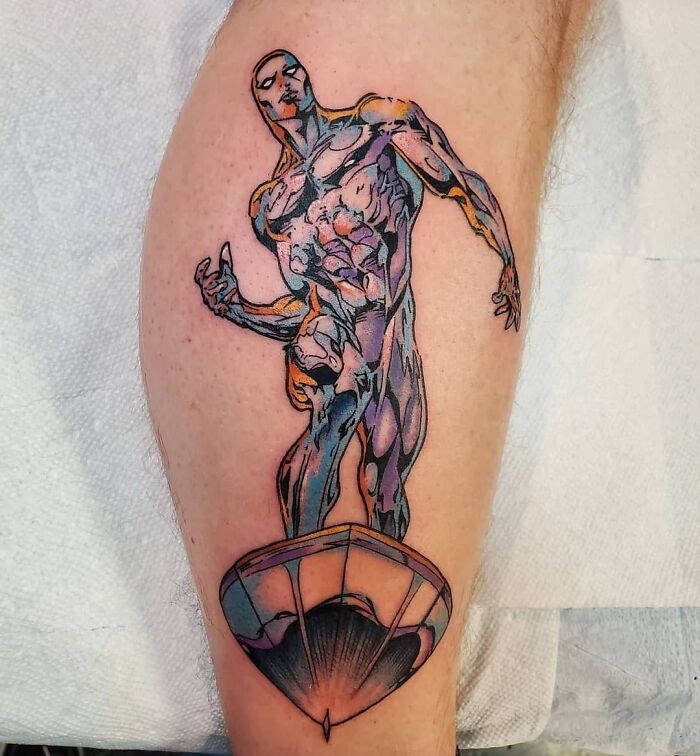 A detailed Marvel tattoo featuring a superhero Silver Surfer in a dynamic pose on a forearm.