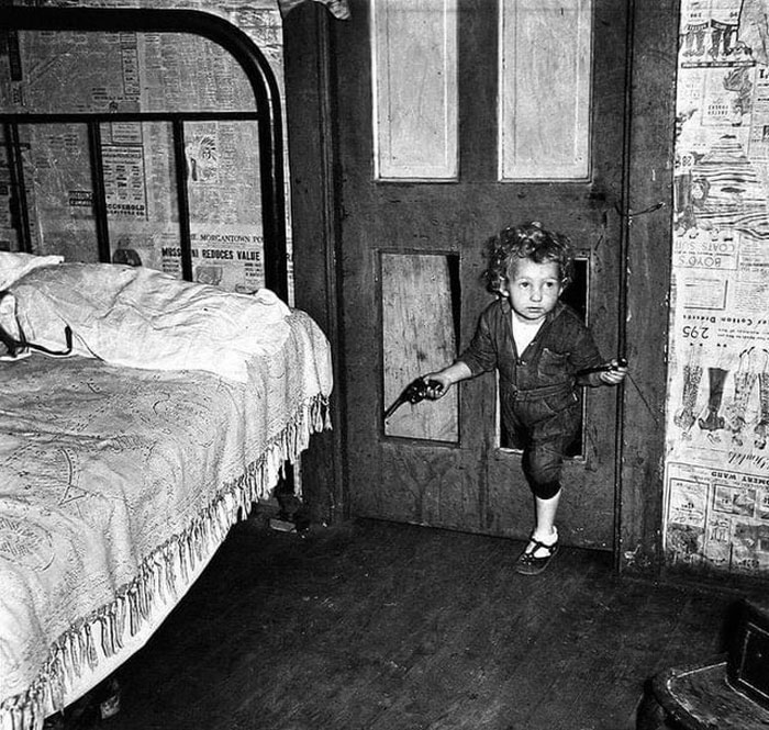 Coal Miner's Child Using A Hole In The Door To Enter A Bedroom With A Smoking Pipe In One Hand And A Gun In The Other In Bertha Hill, West Virginia. Photo By Marion Post Wolcott. 1938
