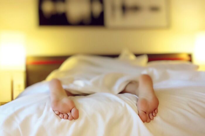 Person Lying In Bed With Feet Coming Out Of Blanket 