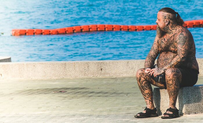 Tattooed Man Sitting Next To A Swimming Pool 