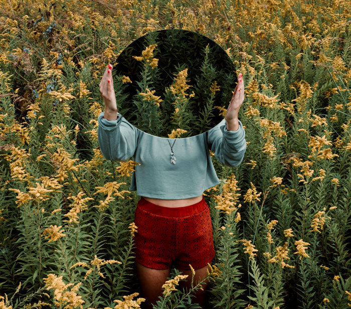 Woman holding mirror in flower field