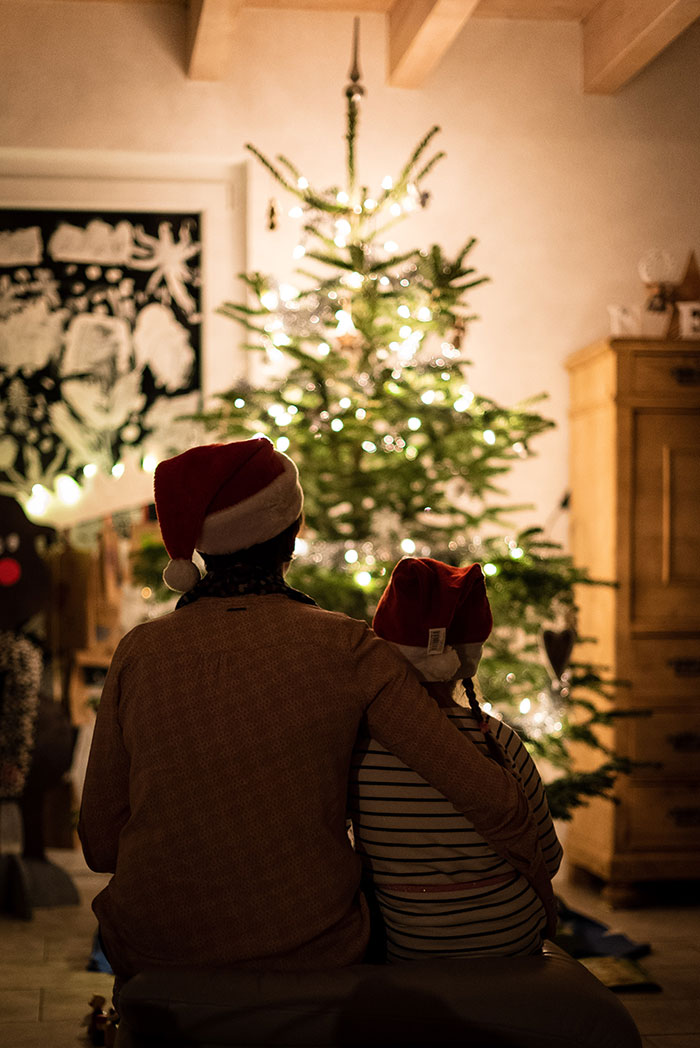 Picture of person and kid sitting and looking at Christmas tree