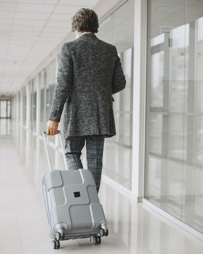 A man in a gray suit walking with his luggage
