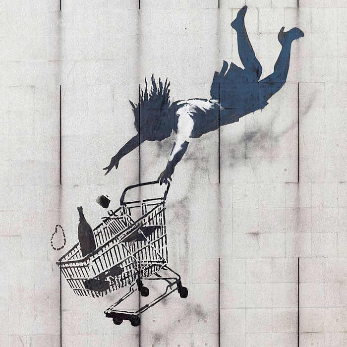 Graffiti of a woman with a shopping trolley falling down the side of a building. Items are falling out of the trolley