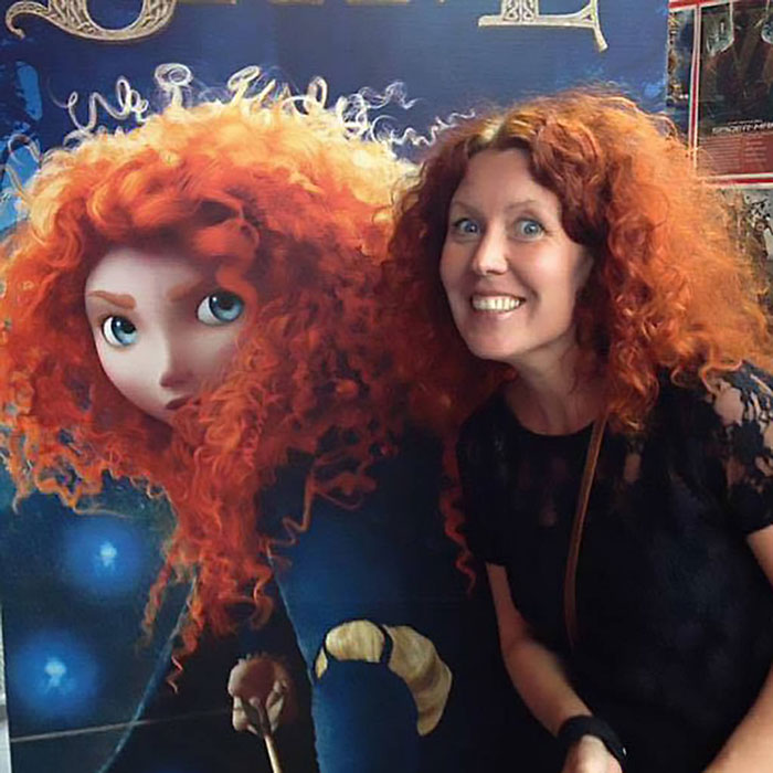 Ginger woman posing in front of a poster of Merida From Brave