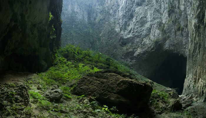 This Cave Entrance At The Bottom Of A Sinkhole In Guizhou, China. See The Four Guys On The Rock For Scale