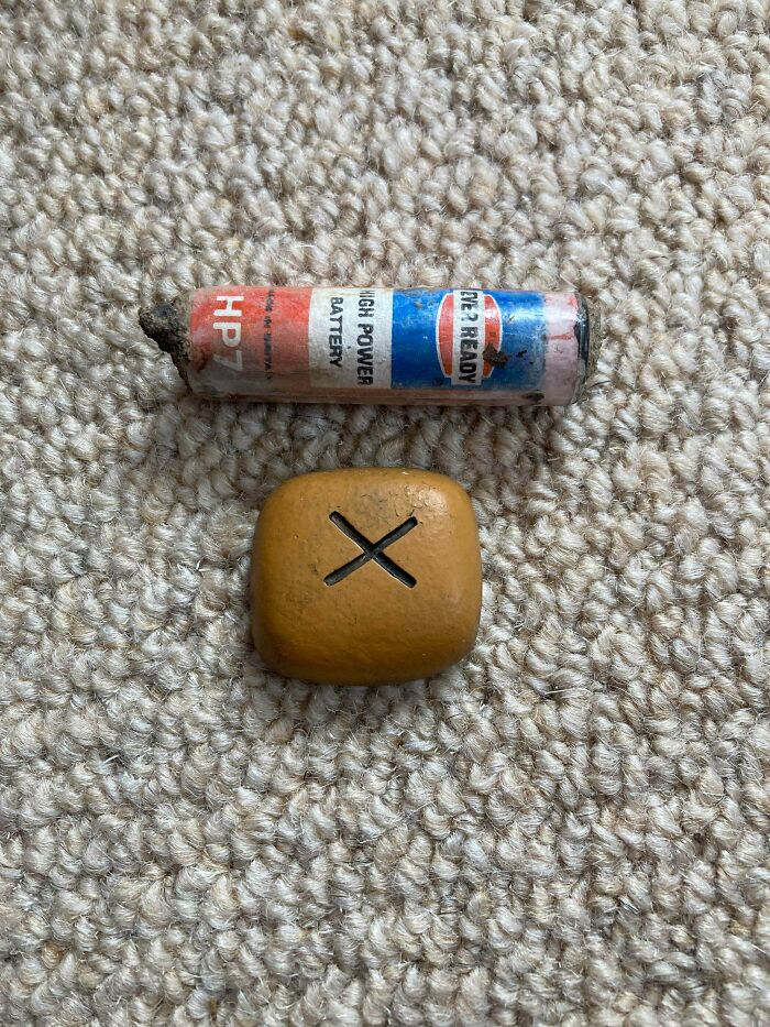 Small, Dense Wood-Effect Plastic Piece With X Slightly Off Centre. No Other Marks. Aa Battery For Scale. Potentially A Game Piece?