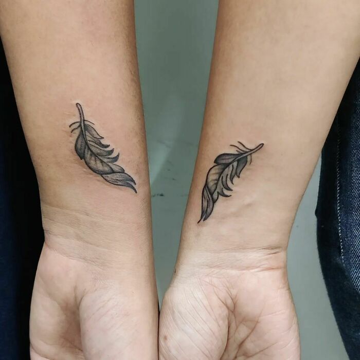 Matching feather best friend tattoos on forearms, symbolizing strong and enduring friendship.