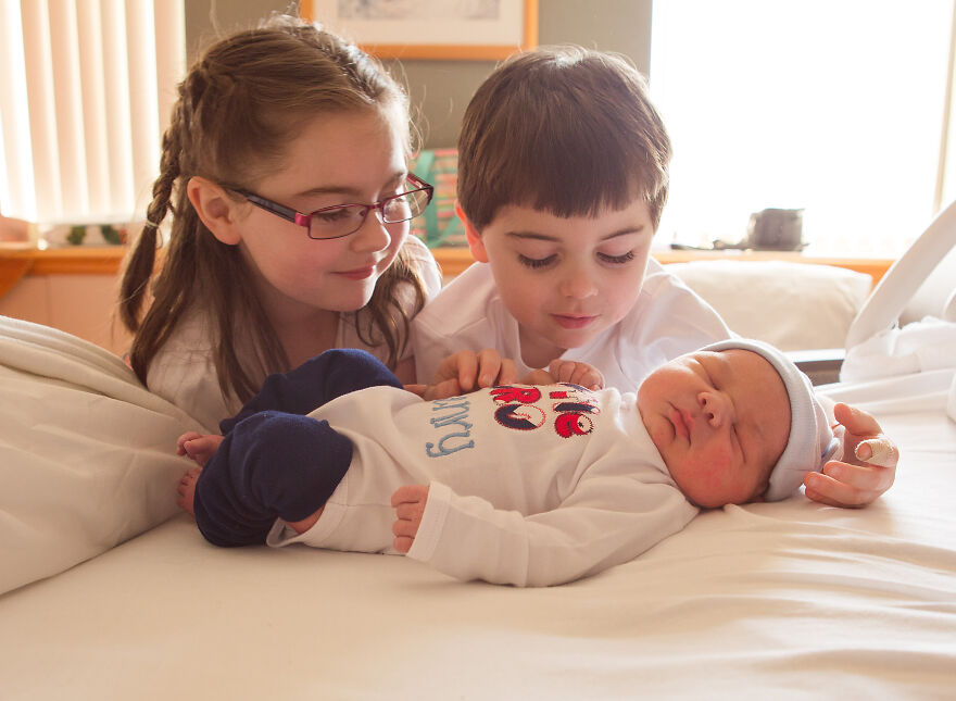 A photograph of a newborn with their siblings