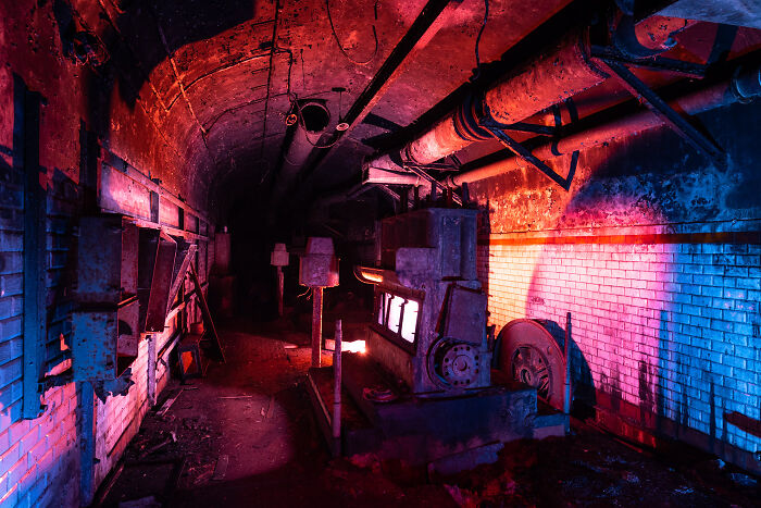 Abandoned place interior at night illuminated with vibrant red and blue light, showcasing industrial pipes and machinery.