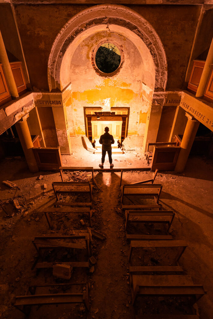 Man standing inside an abandoned place at night illuminated by strong light showing decayed interior and broken benches.