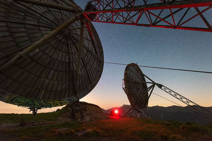 Large abandoned satellite dishes at night under a starry sky, illuminated using a lot of light at an isolated location.