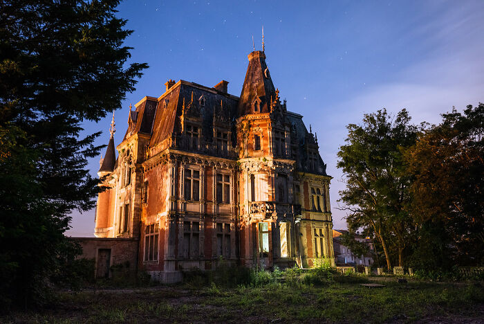 Abandoned place at night illuminated with bright light showcasing aged architecture and surrounding trees under a clear sky.
