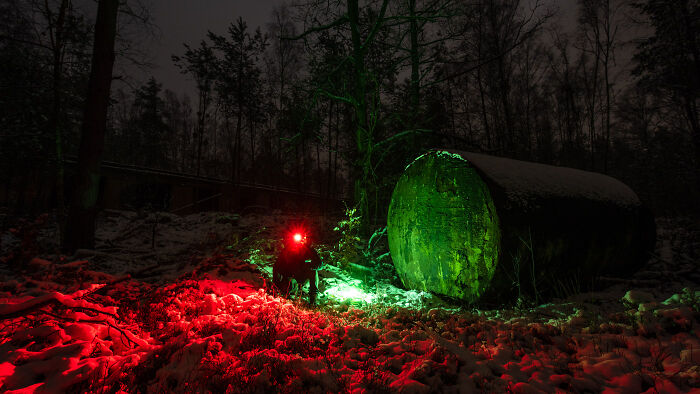 Abandoned place at night illuminated with green and red lights, surrounded by trees and snow-covered terrain.