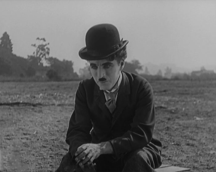 Charlie Chaplin sitting sad in a field 