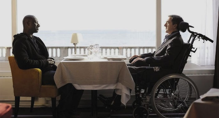 Two people sitting at the table and one is in a wheelchair 