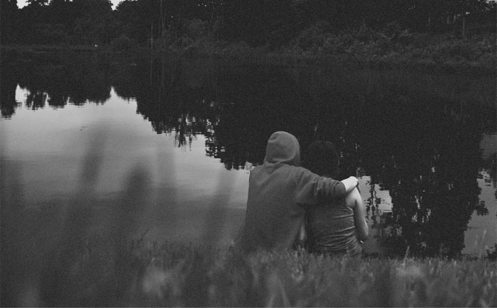Black and white picture of two persons sitting near the lake