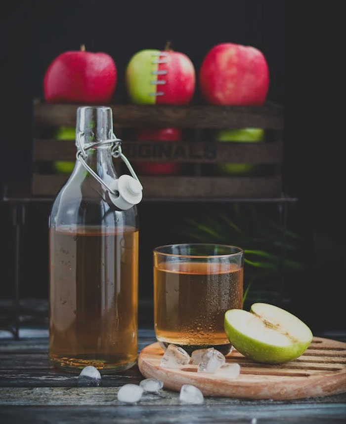 Glass bottle filled with Apple Cider and apples near by 