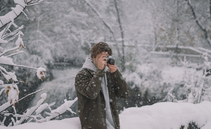 Man taking pictures with a camera while it's snowing 