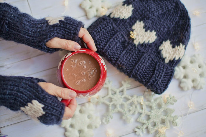 Person in cozy mittens holding a cup of hot chocolate 
